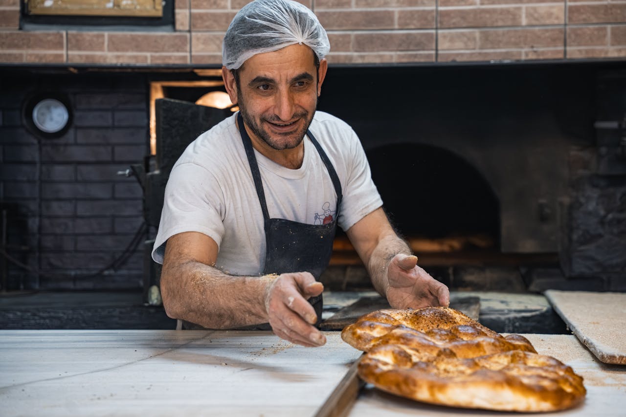 A skilled baker with a cheerful expression, preparing bread in a traditional bakery setting.